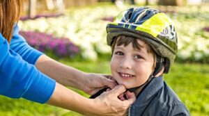 Mother helping cheerful son wearing helmet for cycle