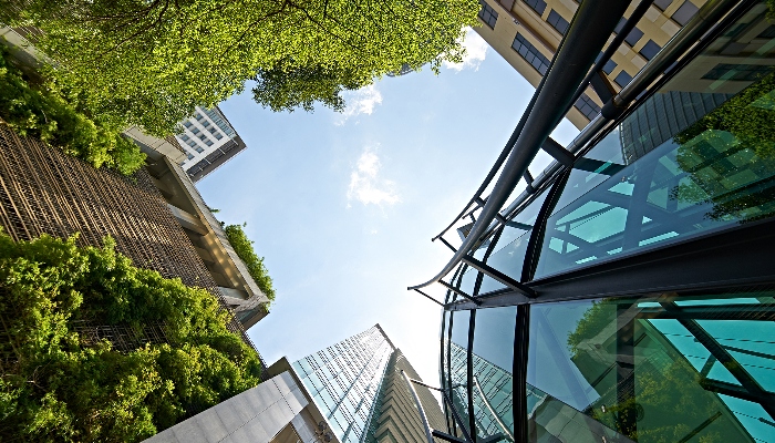 Low angle shot of modern glass buildings and green with clear sky background.