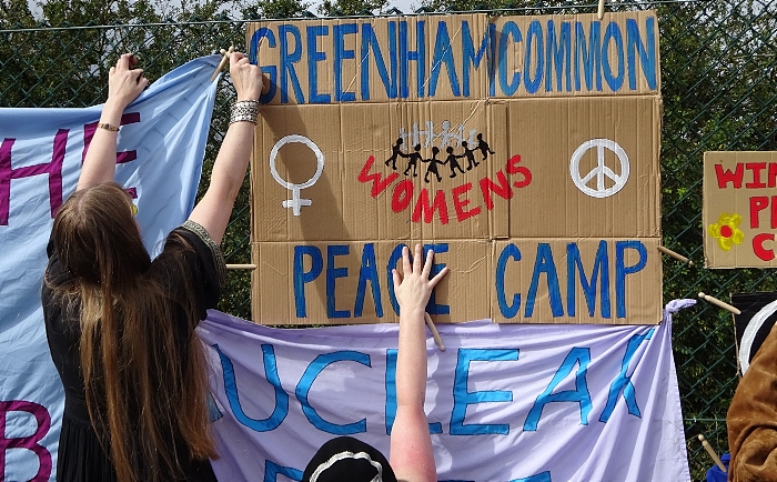 Greenham Common Women’s Peace Camp protestor re-enactors put up signs on perimeter fence (1)