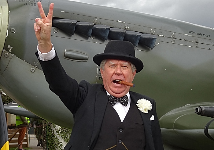 Winston Churchill lookalike gives the V for victory sign in front of a replica Spitfire
